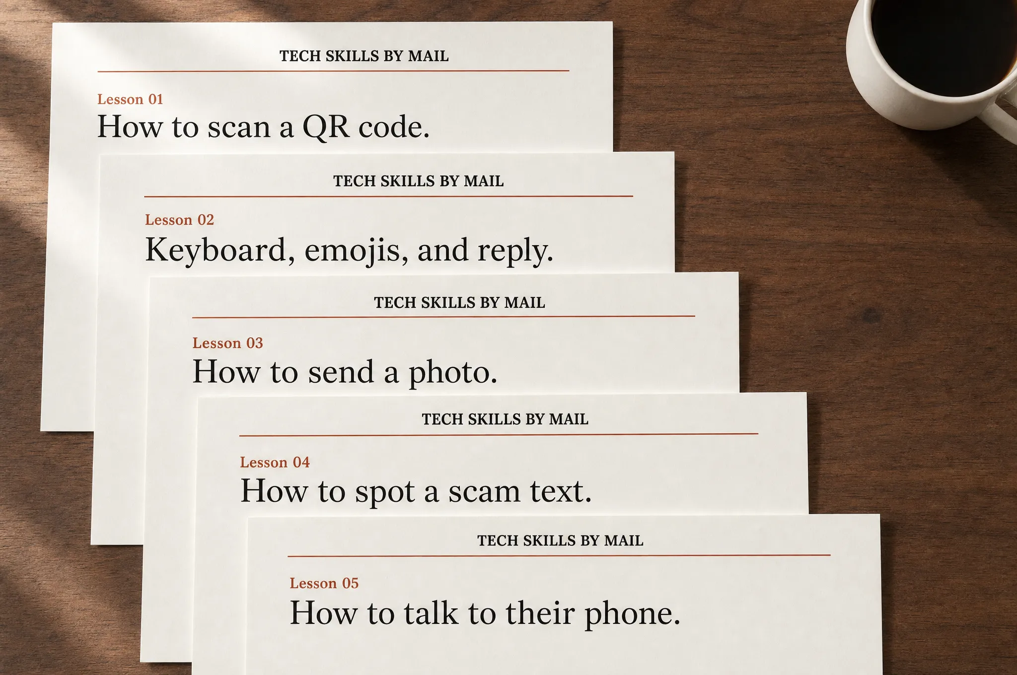 Five Tech Skills by Mail lesson pages cascading on a dark wood counter, a coffee mug in the upper right — each page in plain serif type with a brick-orange rule. Lesson 01: How to scan a QR code. Lesson 02: Keyboard, emojis, and reply. Lesson 03: How to send a photo. Lesson 04: How to spot a scam text. Lesson 05: How to talk to their phone.